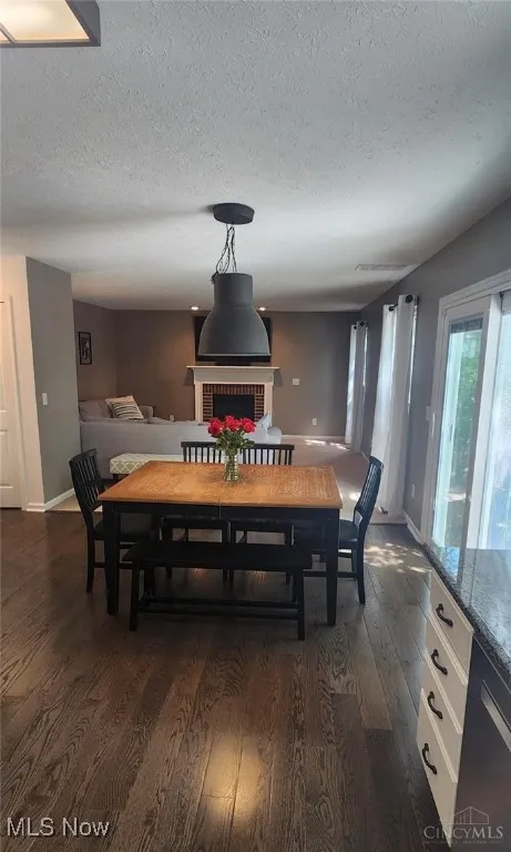 Dining room with dark wood-style flooring, a textured ceiling, and a brick fireplace