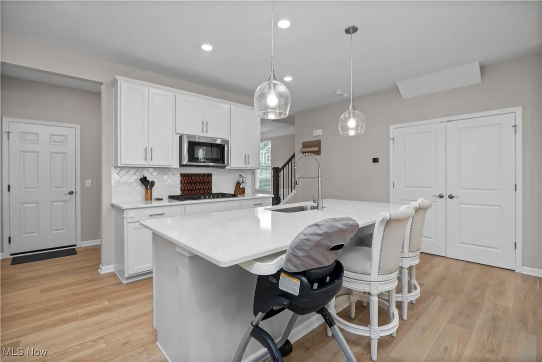 Kitchen featuring white cabinets, decorative backsplash, pendant lighting, a kitchen bar, and light wood-style flooring