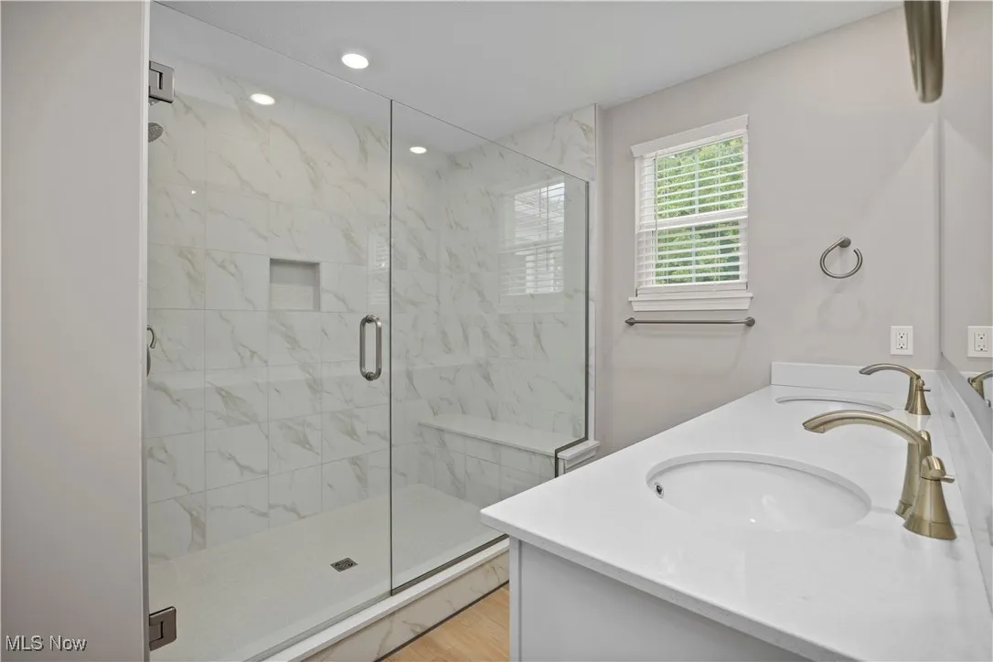 Full bathroom featuring a marble finish shower, double vanity, and recessed lighting