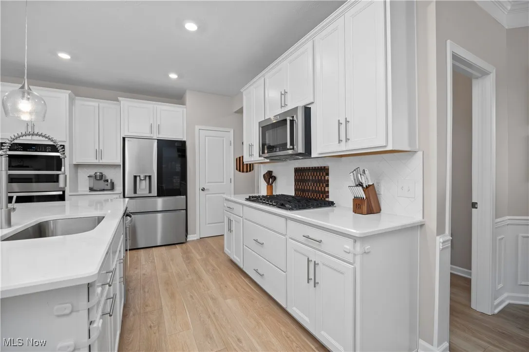Kitchen with decorative light fixtures, decorative backsplash, appliances with stainless steel finishes, white cabinetry, and recessed lighting