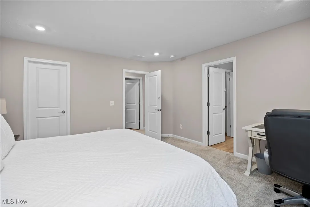 Bedroom with light colored carpet, recessed lighting, and a desk