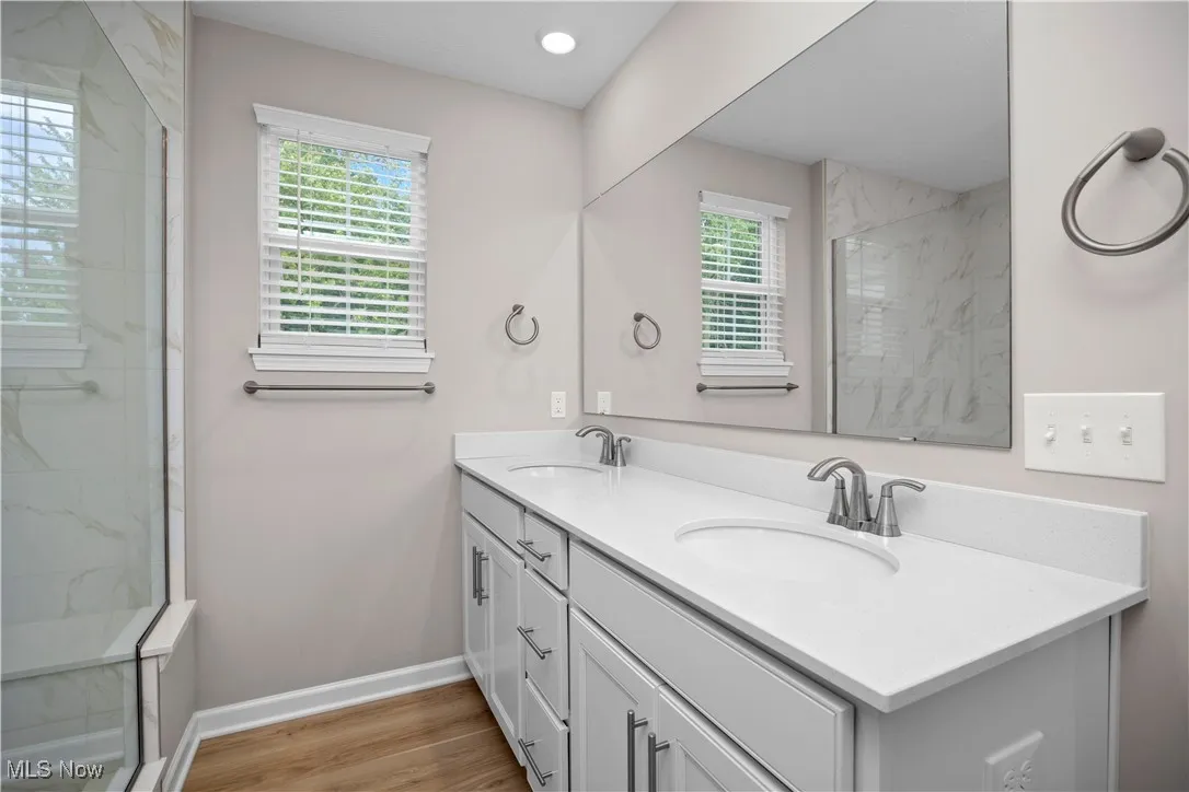 Bathroom featuring double vanity, light wood-type flooring, a marble finish shower, and recessed lighting