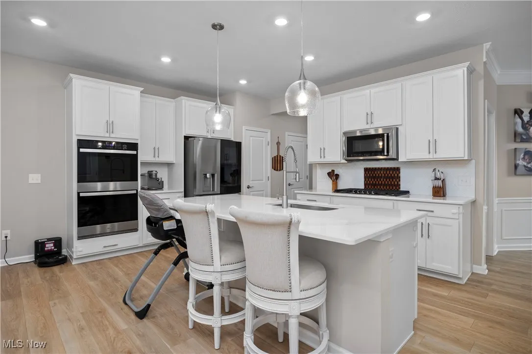 Kitchen with white cabinets, appliances with stainless steel finishes, a breakfast bar, tasteful backsplash, and light wood-type flooring
