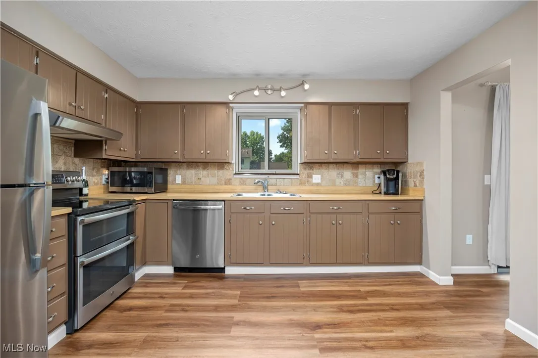 Kitchen featuring appliances with stainless steel finishes, light countertops, backsplash, under cabinet range hood, and light wood finished floors