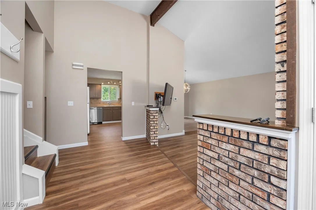 Hallway featuring beam ceiling, wood finished floors, high vaulted ceiling, and stairway