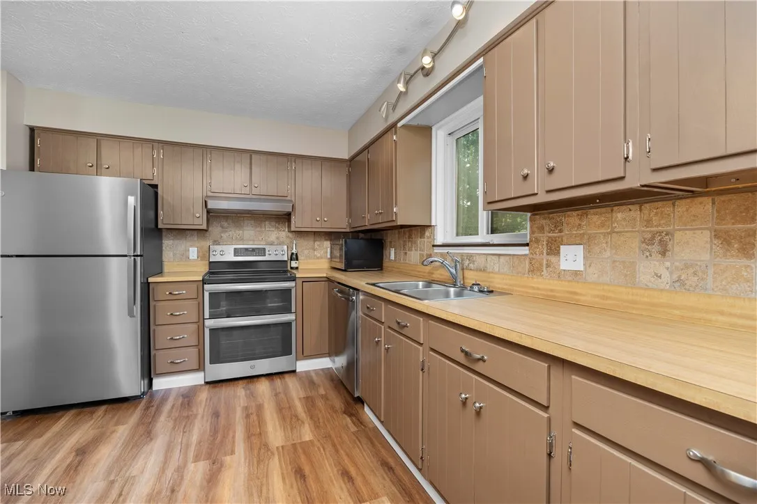 Kitchen featuring stainless steel appliances, light countertops, light wood-style floors, a textured ceiling, and backsplash