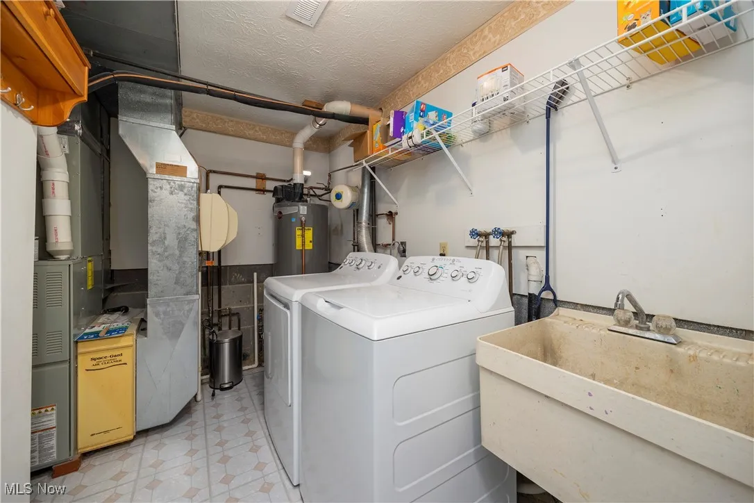 Laundry area with a textured ceiling, heating unit, washer and clothes dryer, and water heater