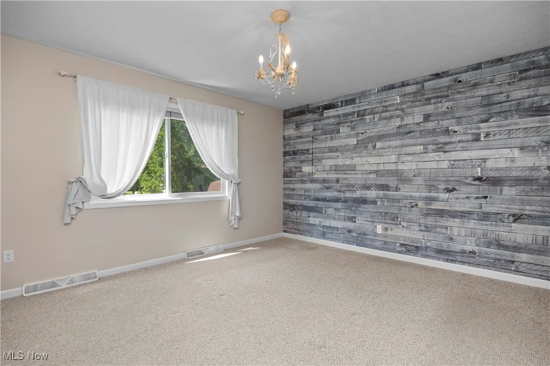 Unfurnished room featuring wood walls, carpet, a chandelier, and an accent wall