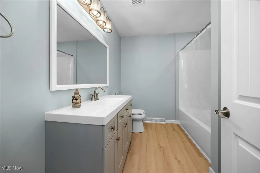 Full bathroom with light wood-type flooring, shower / tub combo with curtain, and vanity