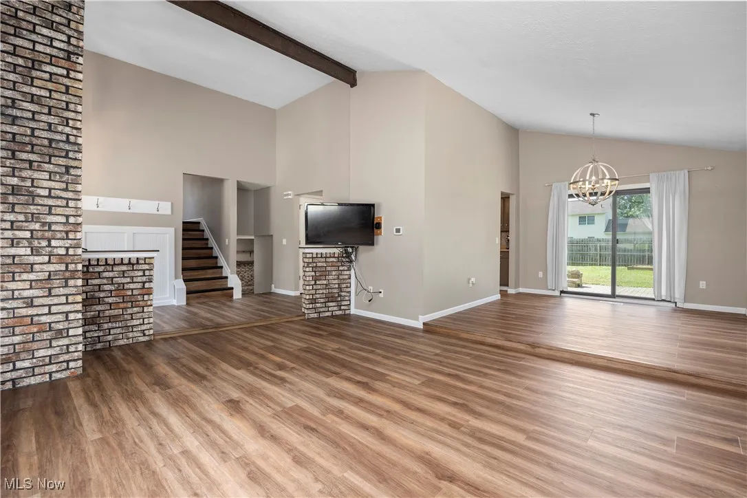 Unfurnished living room featuring wood finished floors, a chandelier, beam ceiling, high vaulted ceiling, and stairway