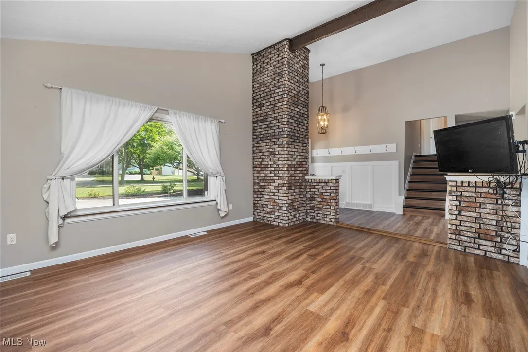 Unfurnished living room with wood finished floors, high vaulted ceiling, beamed ceiling, and stairs