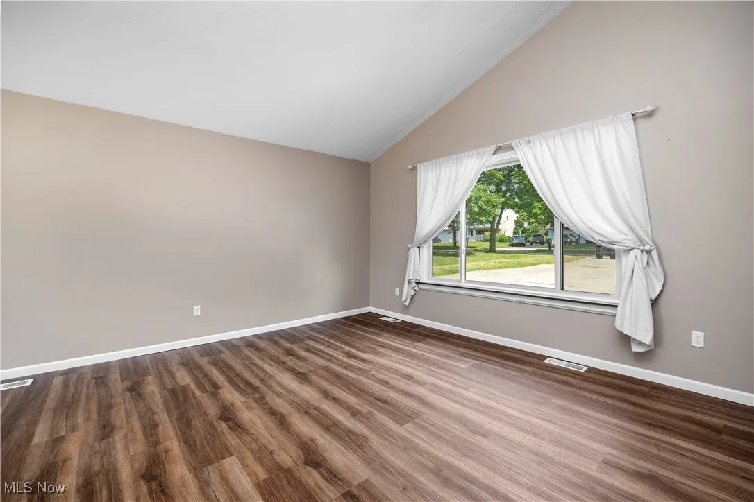 Spare room featuring dark wood-style flooring and lofted ceiling