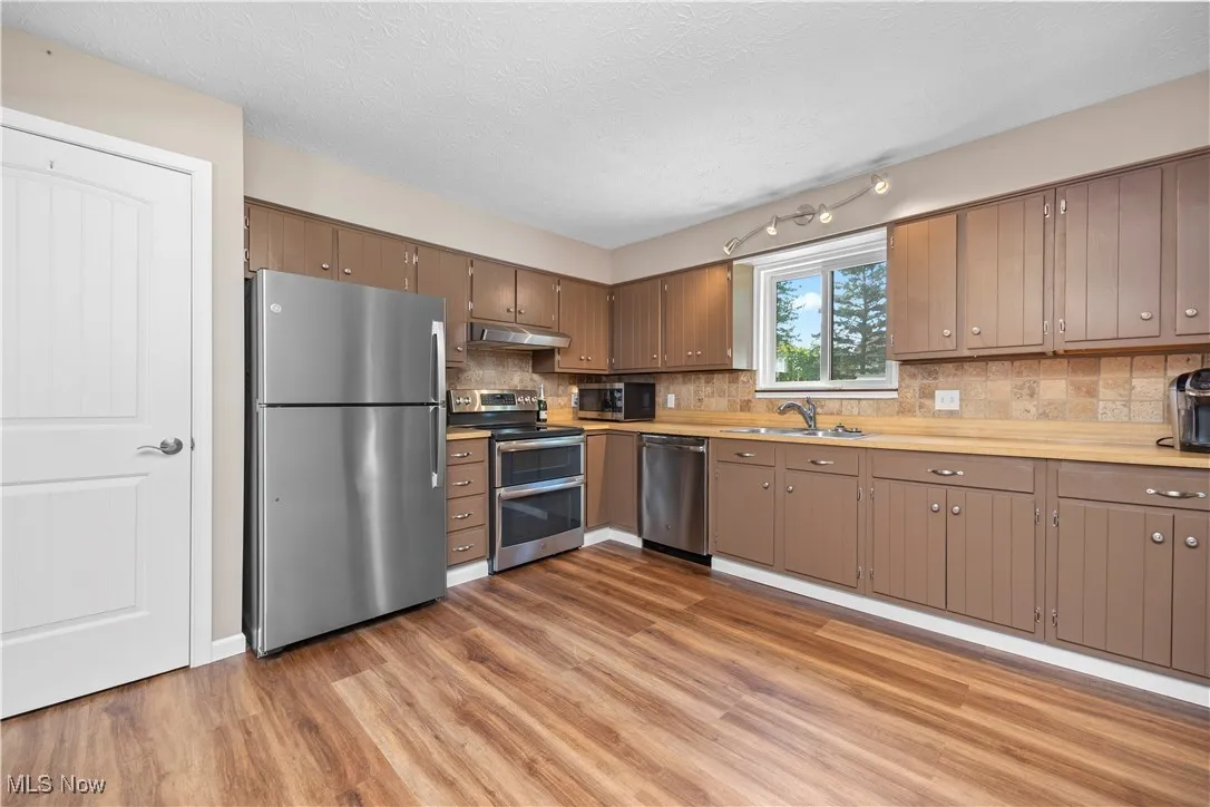 Kitchen featuring stainless steel appliances, a textured ceiling, light wood finished floors, tasteful backsplash, and under cabinet range hood