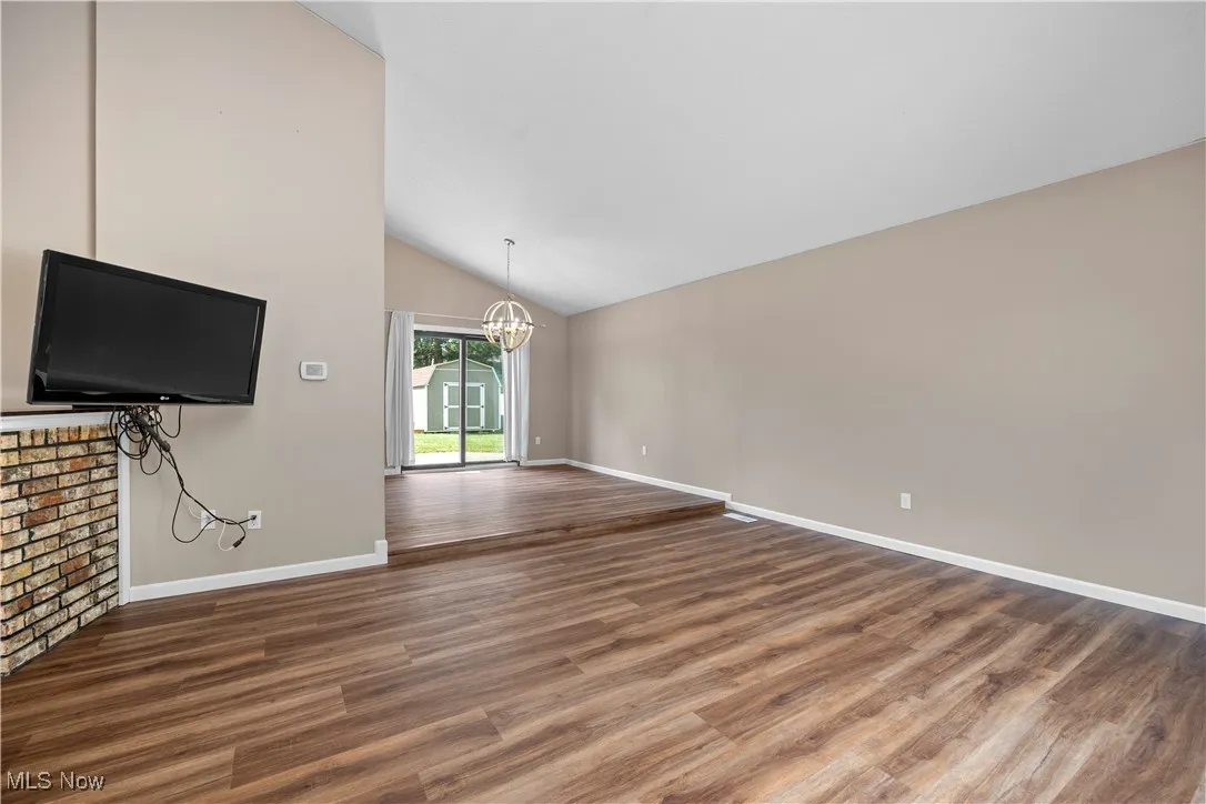 Unfurnished living room with a chandelier, dark wood-type flooring, and high vaulted ceiling