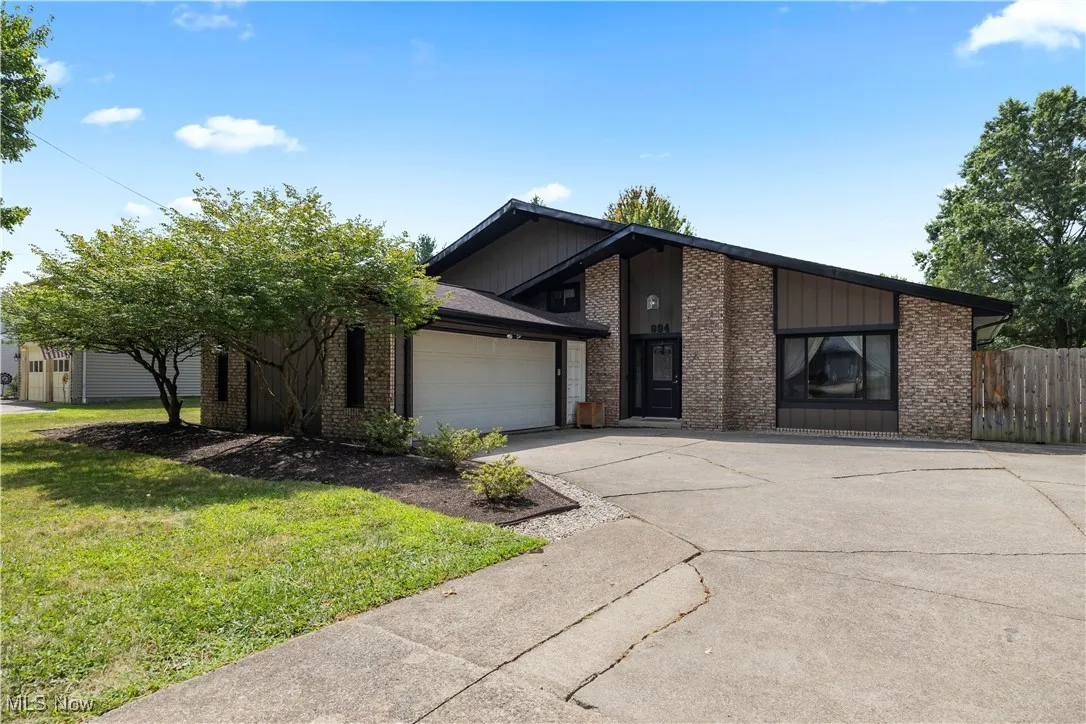 Mid-century home with concrete driveway, a garage, brick siding, and a front yard