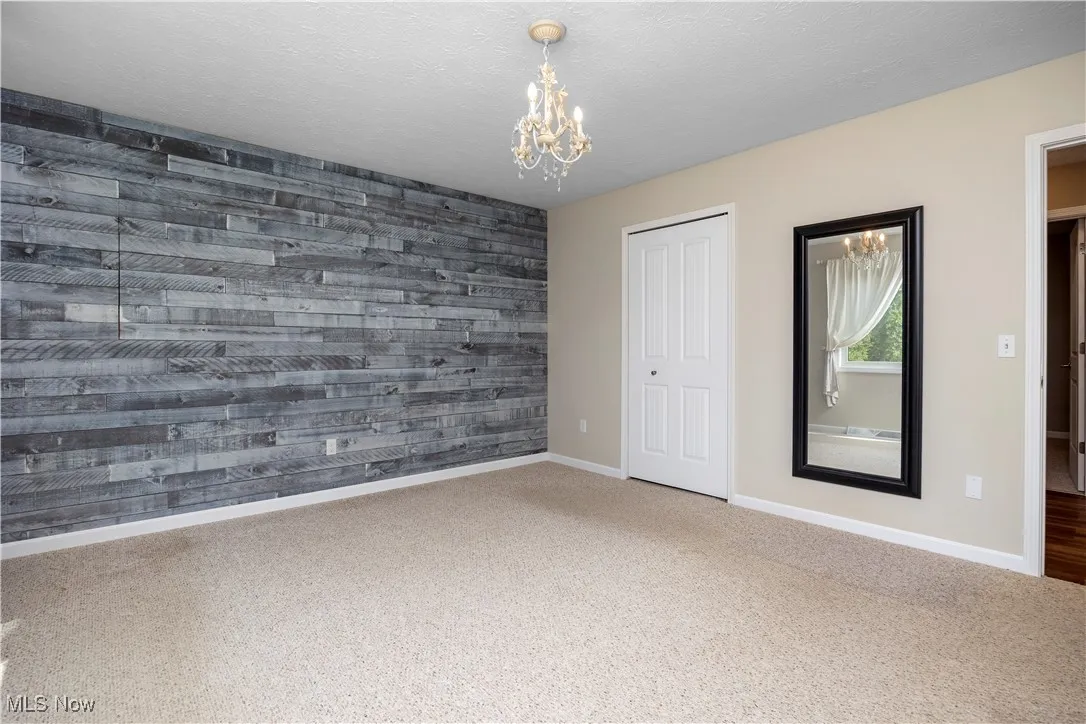 Unfurnished bedroom with wood walls, a chandelier, a textured ceiling, a closet, and carpet floors