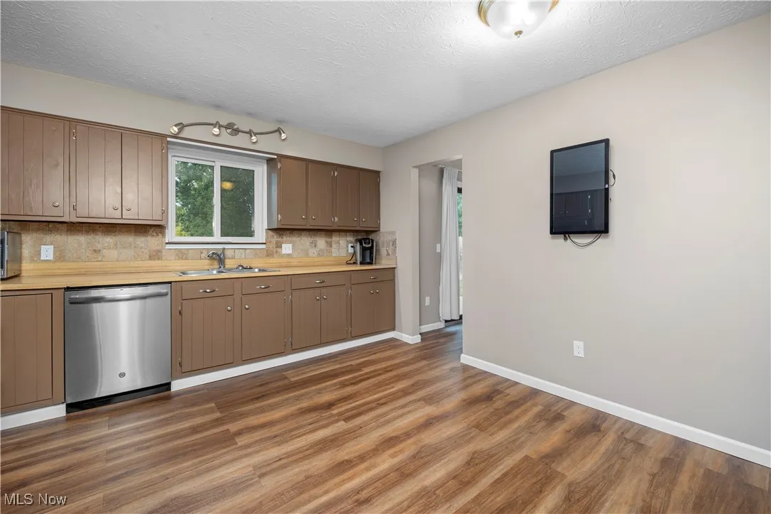 Kitchen with light countertops, dishwasher, decorative backsplash, a textured ceiling, and dark wood-type flooring