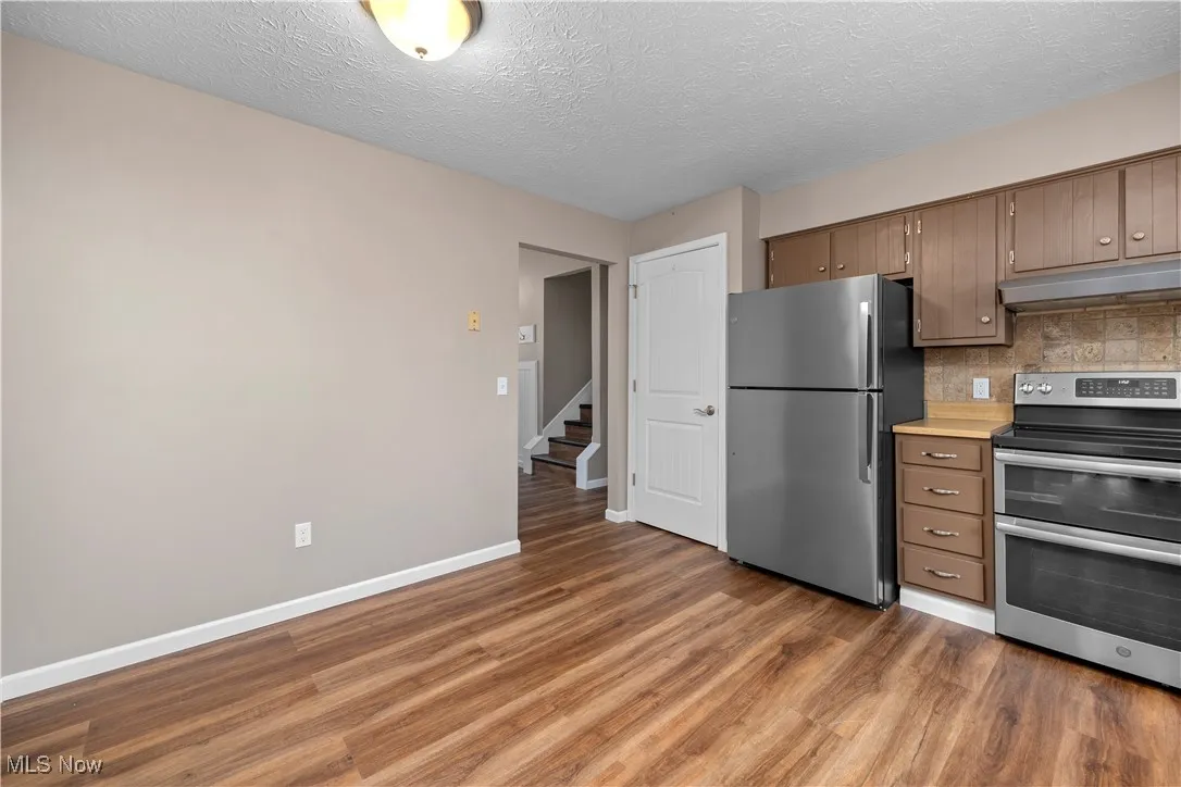 Kitchen featuring stainless steel appliances, under cabinet range hood, backsplash, dark wood-style floors, and light countertops