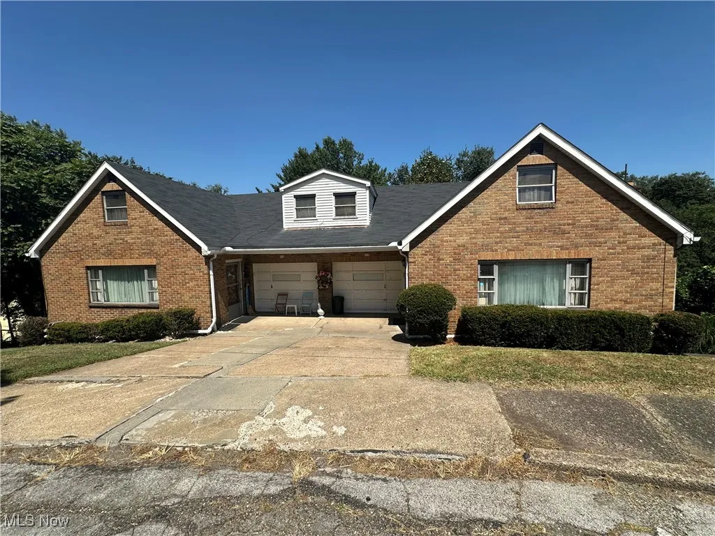 View of front facade featuring brick siding, driveway, an attached garage, and roof with shingles