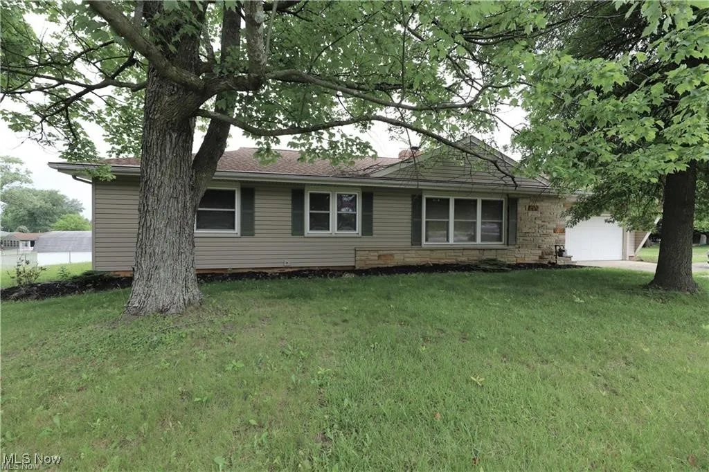 View of front of property with a garage, a front yard, stone siding, and roof with shingles