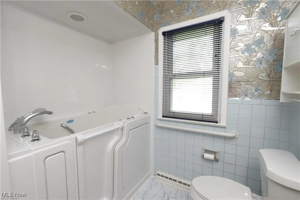 Full bath featuring wallpapered walls, a bath, tile walls, and baseboard heating
