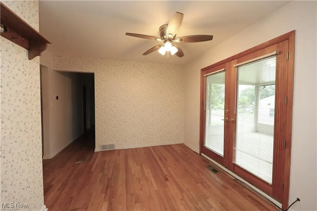 Empty room featuring wood finished floors, french doors, a ceiling fan, and wallpapered walls