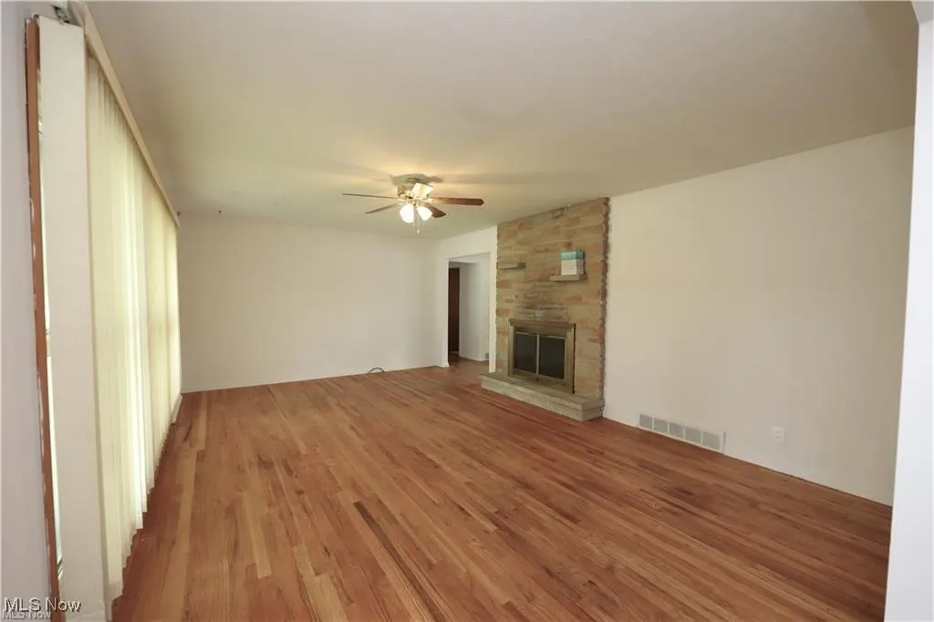 Unfurnished living room featuring wood finished floors, a stone fireplace, and ceiling fan