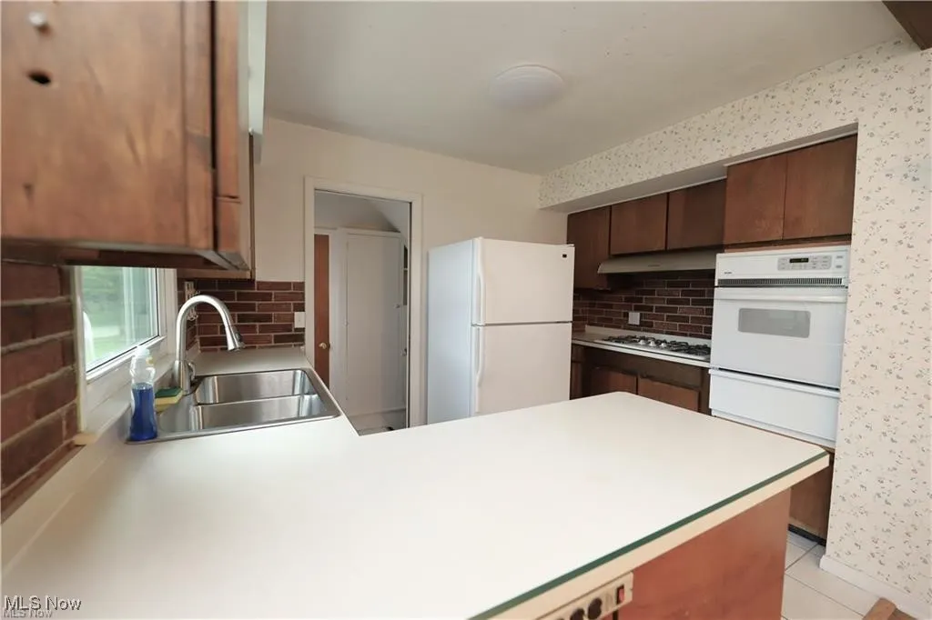 Kitchen featuring light countertops, white appliances, backsplash, a peninsula, and a warming drawer