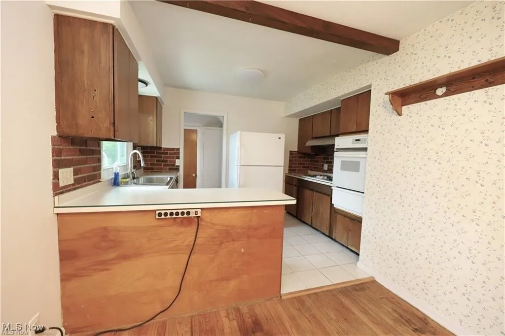 Kitchen featuring light countertops, brown cabinets, light wood finished floors, decorative backsplash, and beamed ceiling