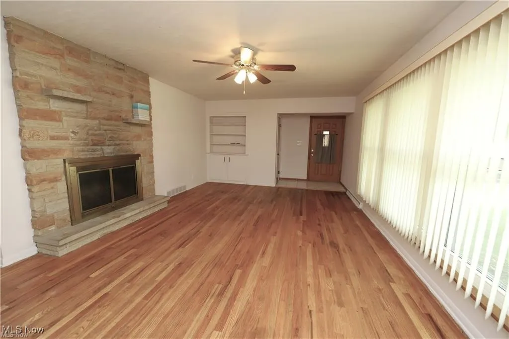 Unfurnished living room featuring a stone fireplace, light wood finished floors, and a ceiling fan
