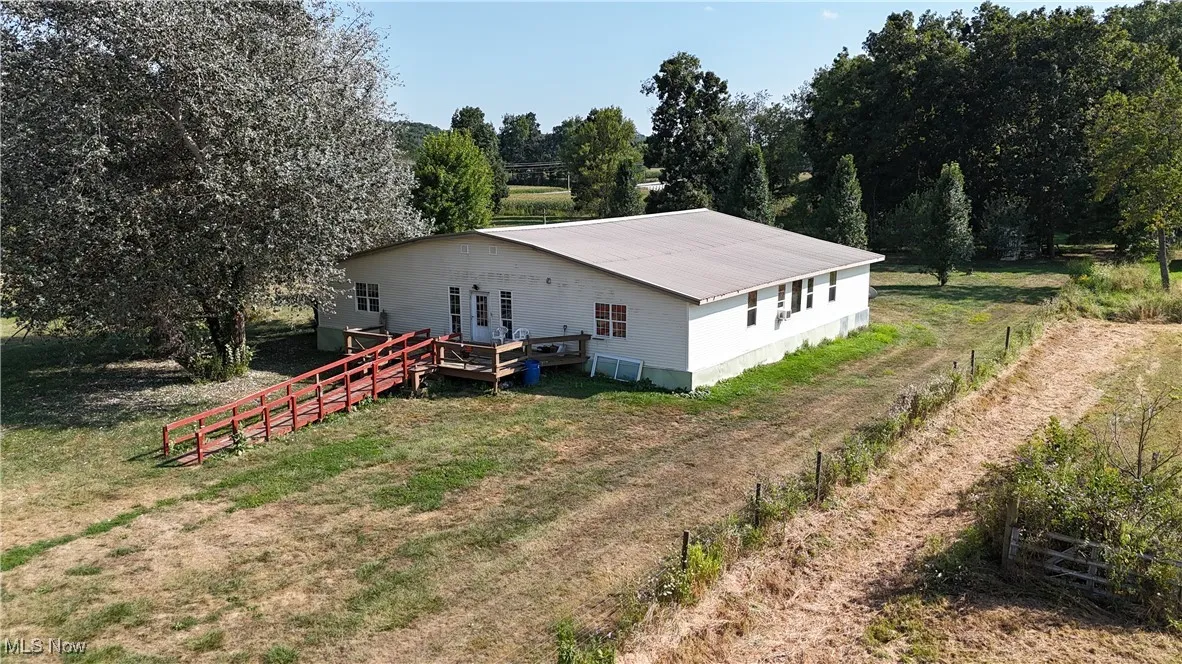 Rear view of property with a lawn, a metal roof, view of wooded area, and a wooden deck