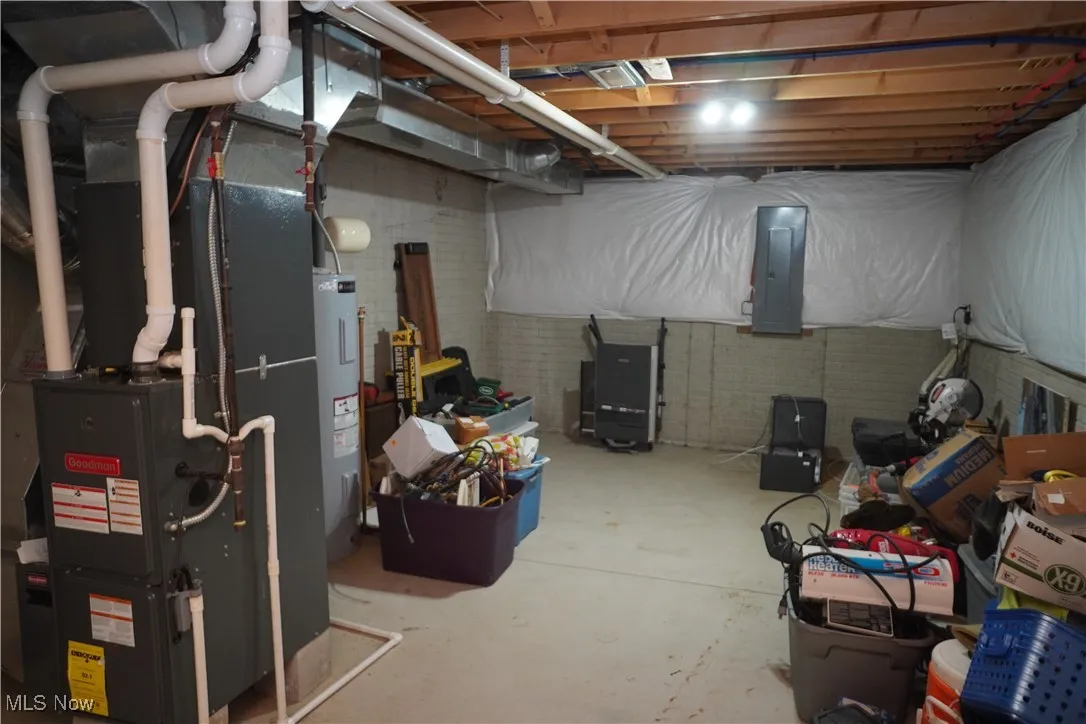 Unfinished below grade area with heating unit, electric panel, and electric water heater