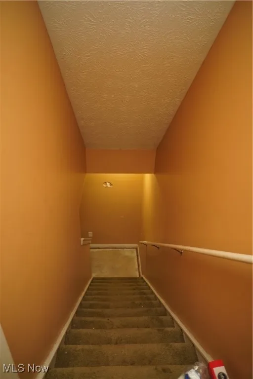 Staircase with carpet and a textured ceiling