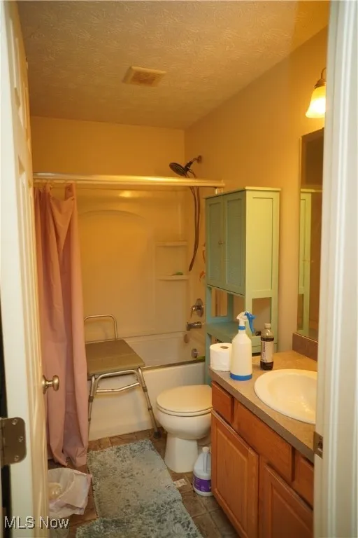 Bathroom with a textured ceiling, shower / bathtub combination with curtain, vanity, and dark tile patterned floors