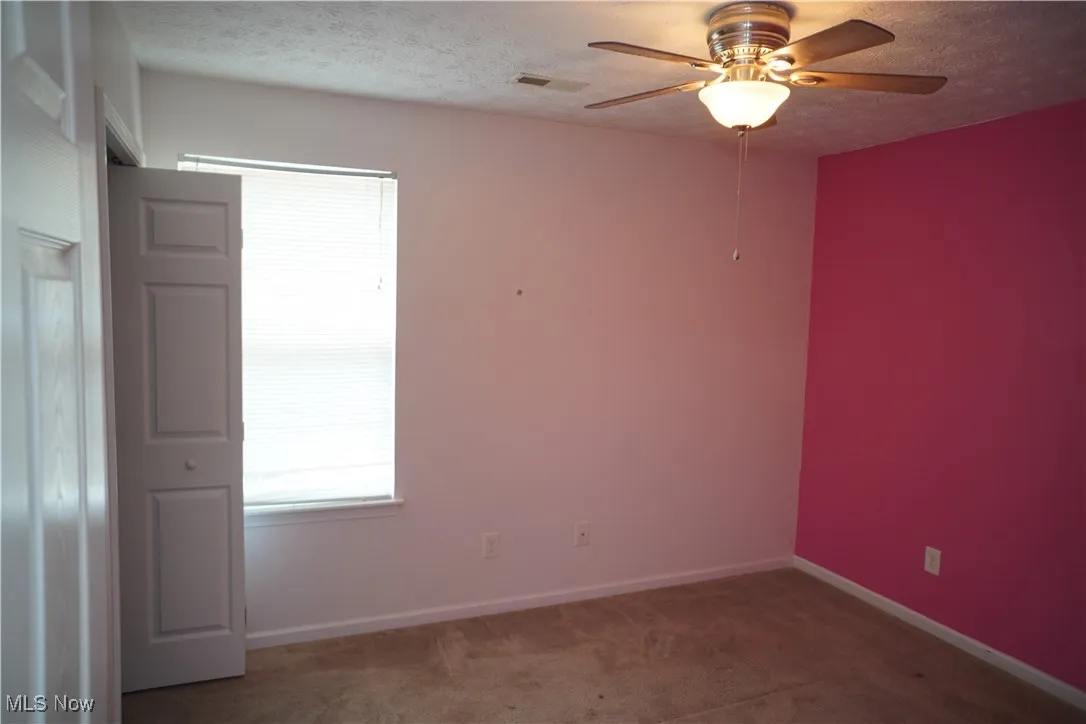 Carpeted empty room featuring a textured ceiling, healthy amount of natural light, and a ceiling fan
