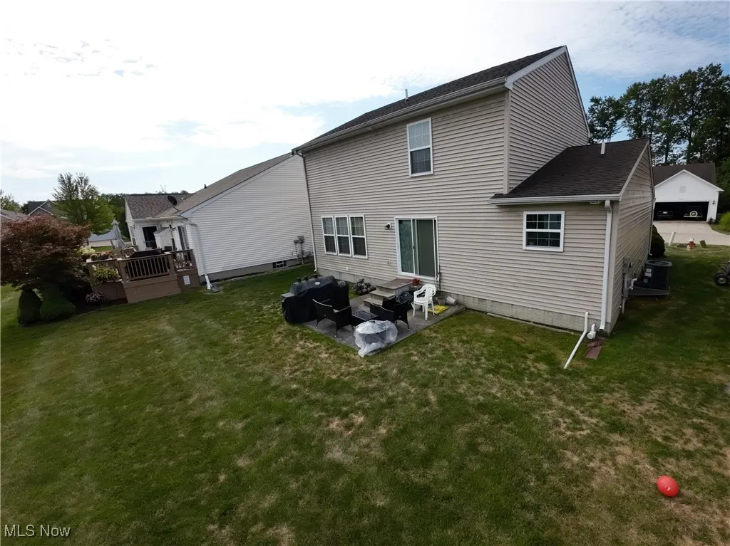 Rear view of house featuring a yard, a wooden deck, a patio area, and a shingled roof