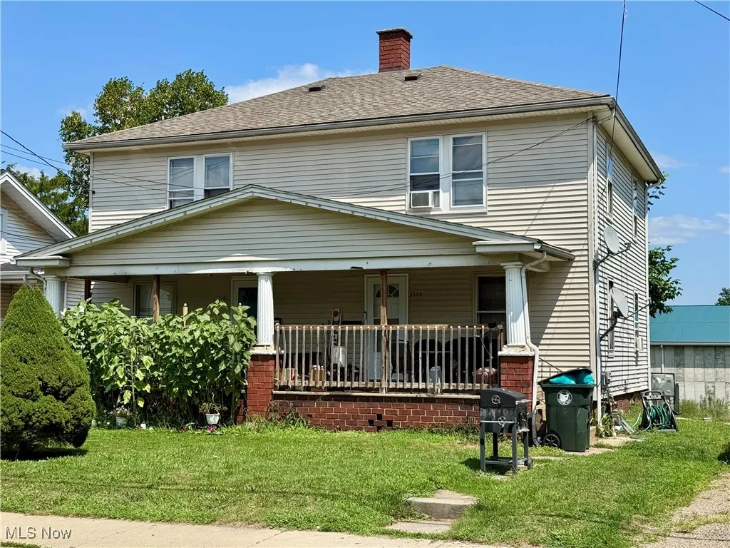 Traditional style home with a front yard, covered porch, a chimney, and a shingled roof