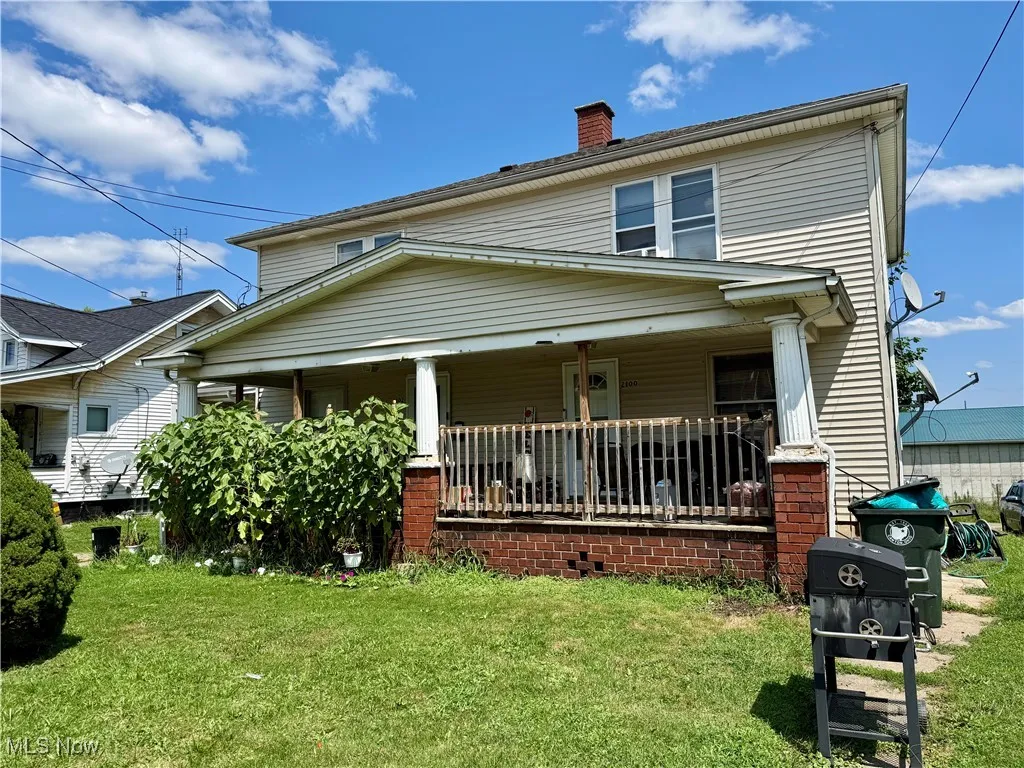 View of front facade featuring a chimney, a front lawn, and covered porch