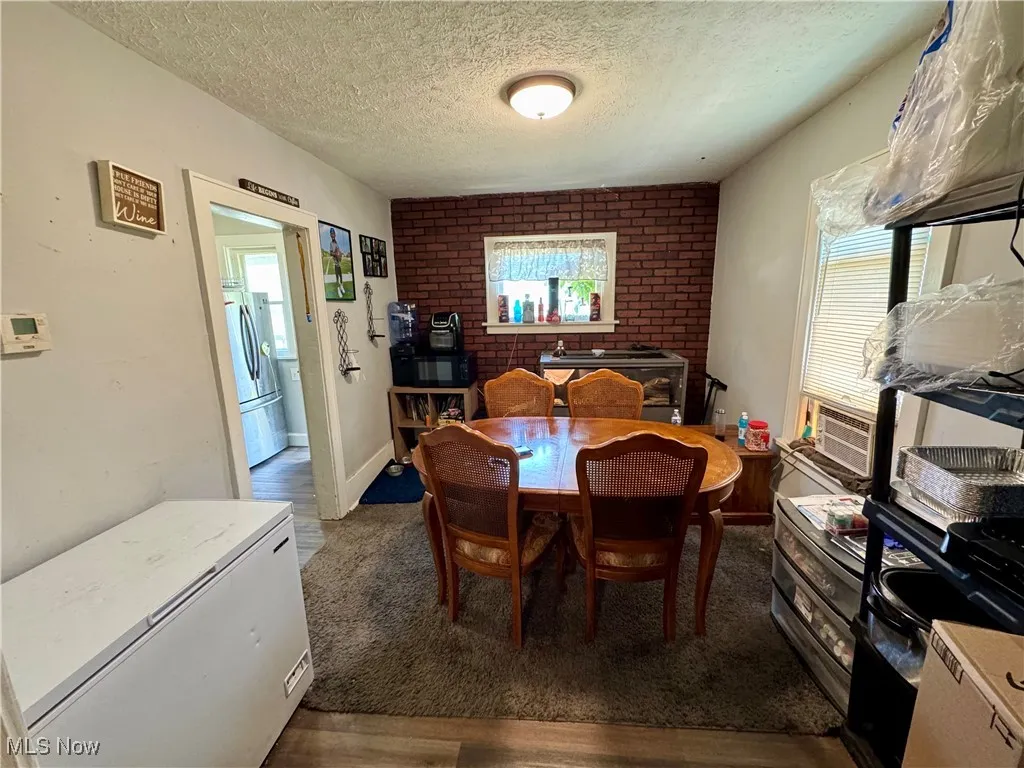Dining area featuring dark wood-style flooring, brick wall, and a textured ceiling