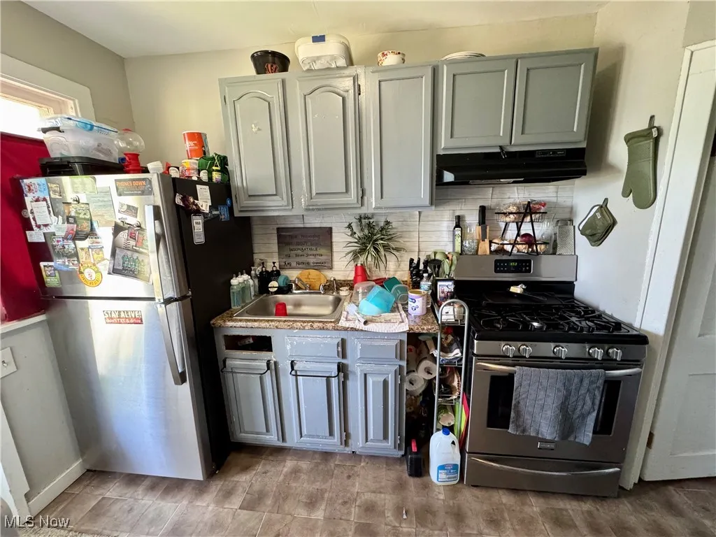 Kitchen featuring stainless steel appliances, decorative backsplash, under cabinet range hood, and light countertops