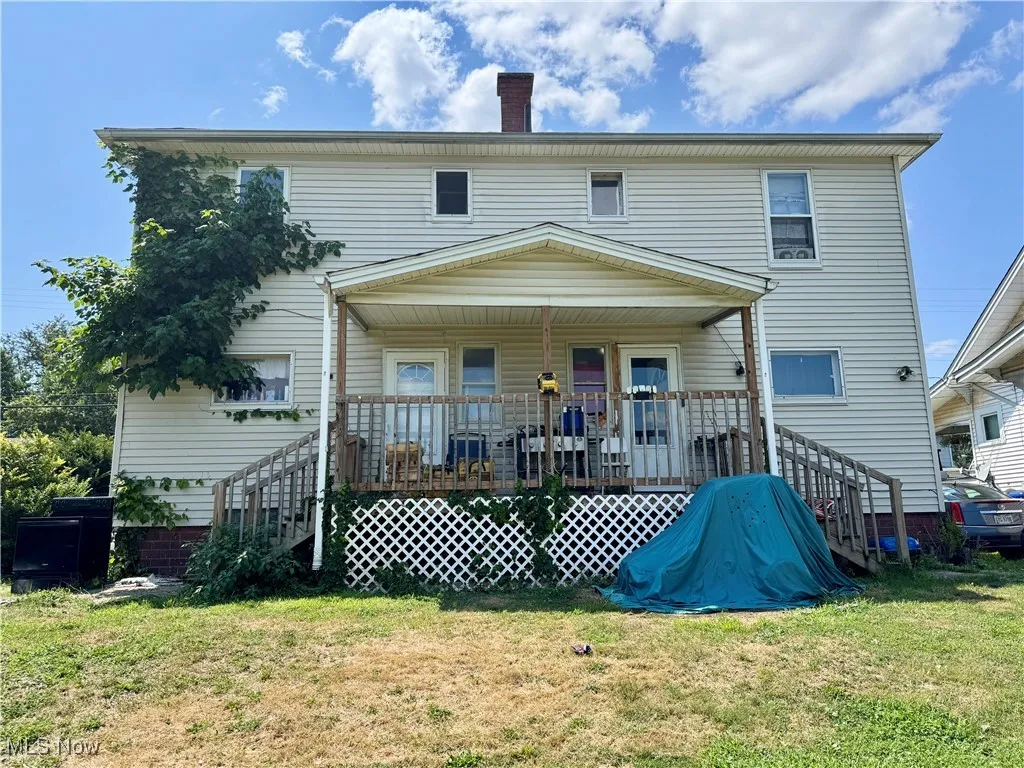 Back of property featuring a yard, stairs, a chimney, and covered porch