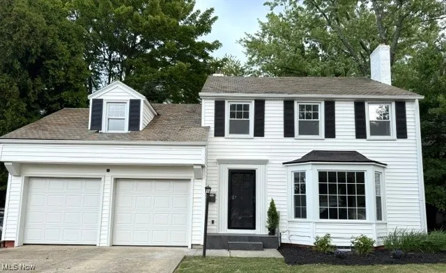 Colonial house featuring an attached garage, a chimney, driveway, and view of wooded area