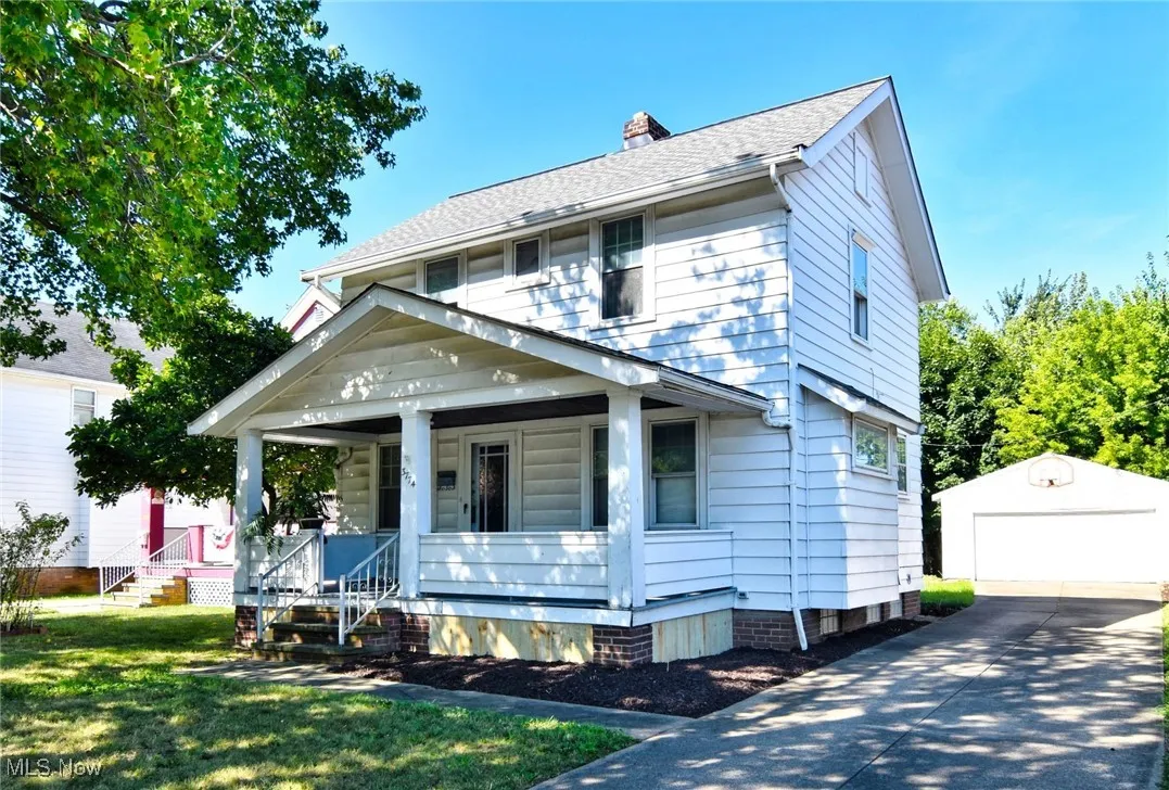 American foursquare style home with covered porch, a detached garage, an outbuilding, a chimney, and a shingled roof