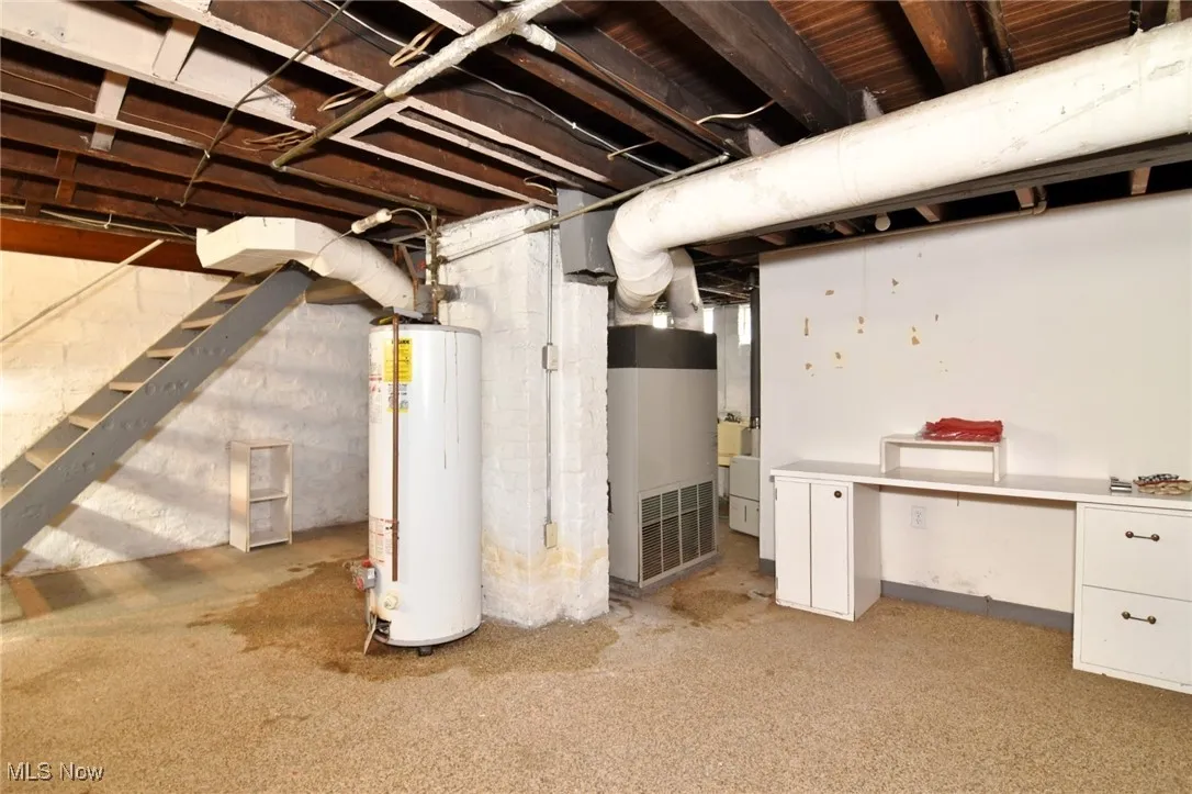 Unfinished basement with gas water heater, stairs, and heating unit