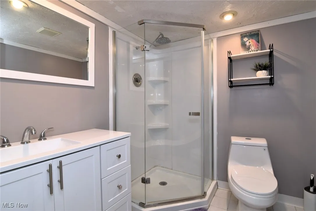 Bathroom featuring a textured ceiling, a shower stall, vanity, and light tile patterned flooring