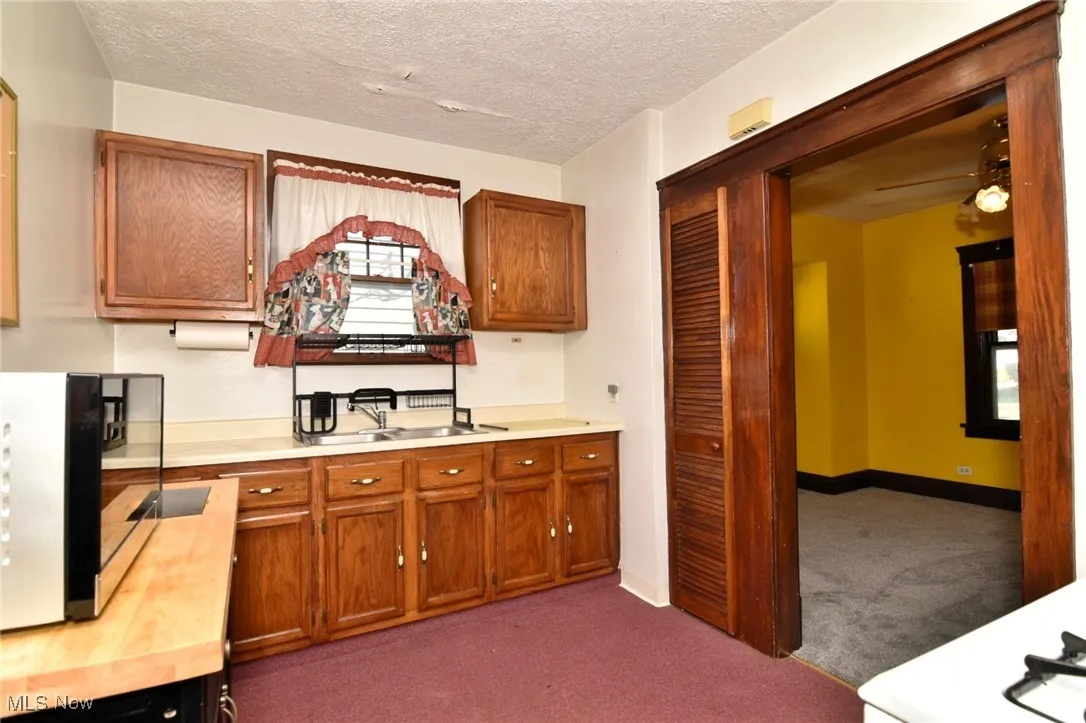 Kitchen featuring light countertops, dark carpet, brown cabinets, a textured ceiling, and black microwave