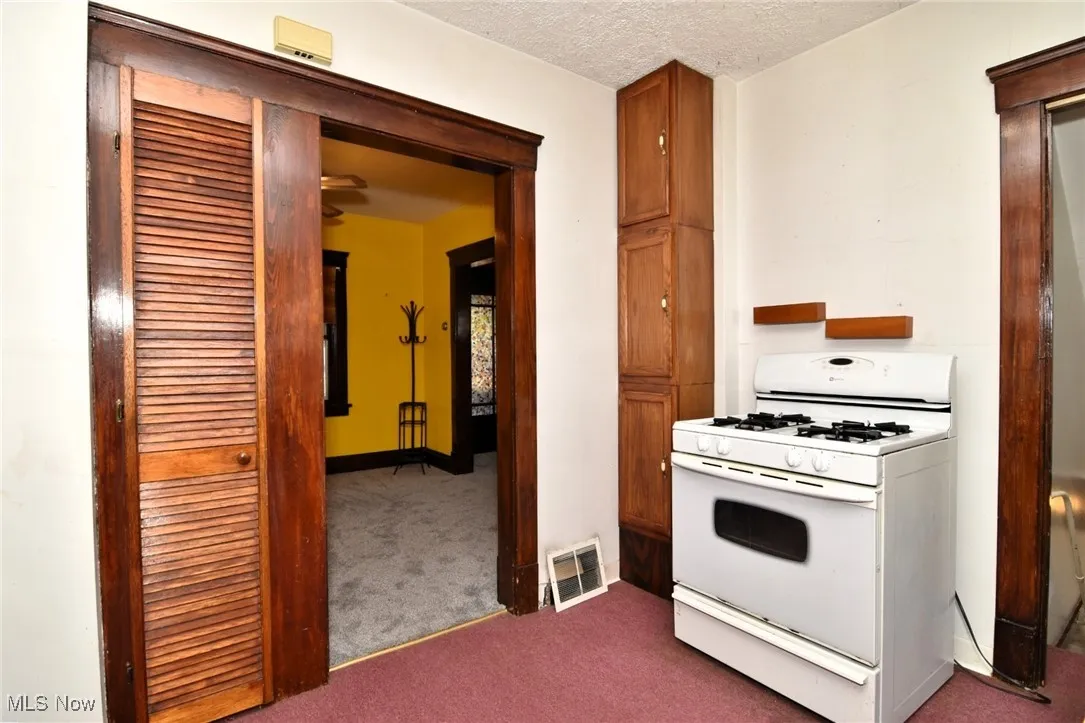 Kitchen featuring white range with gas stovetop, carpet floors, a textured ceiling, and brown cabinets