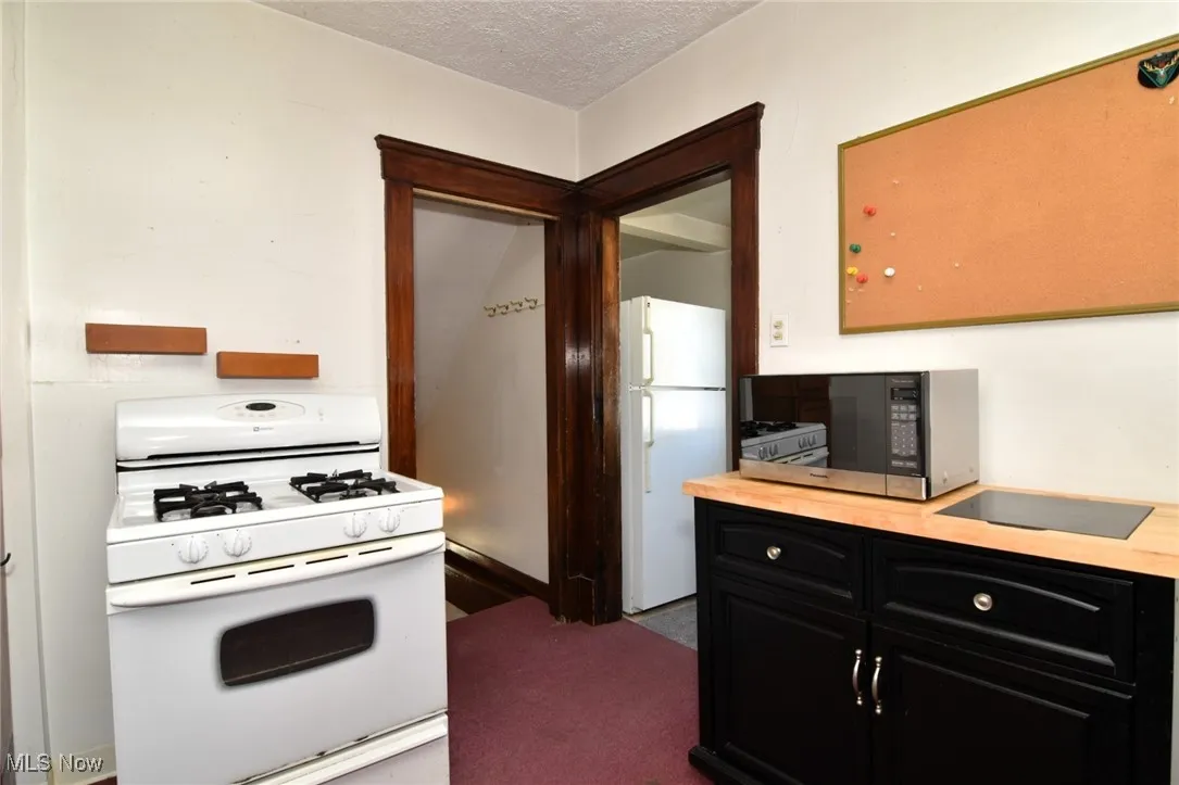 Kitchen with white appliances, dark cabinets, a textured ceiling, dark colored carpet, and butcher block countertops