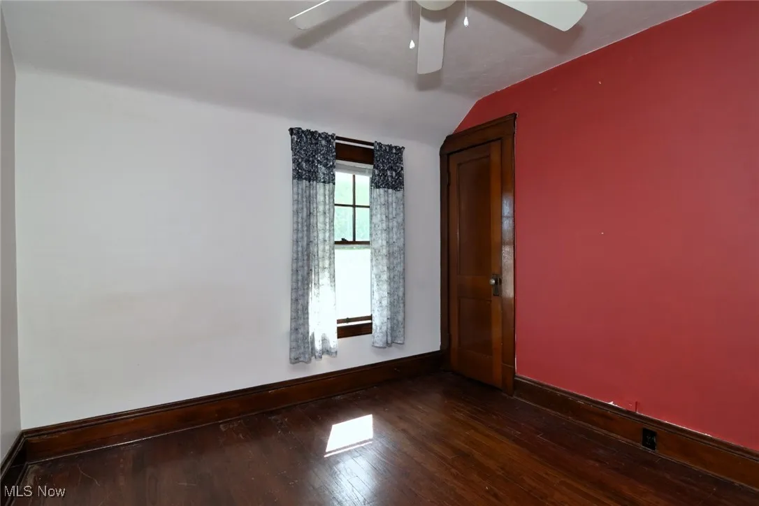 Empty room with dark wood-type flooring, lofted ceiling, and ceiling fan