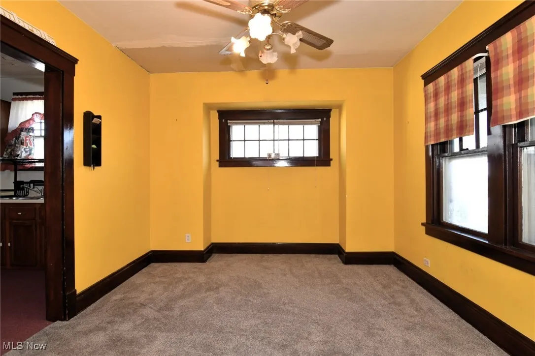 Empty room with dark colored carpet and a ceiling fan
